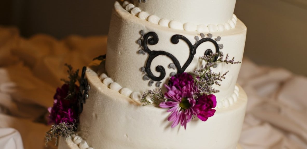 An elegant wedding cake with white frosting and purple flowers.