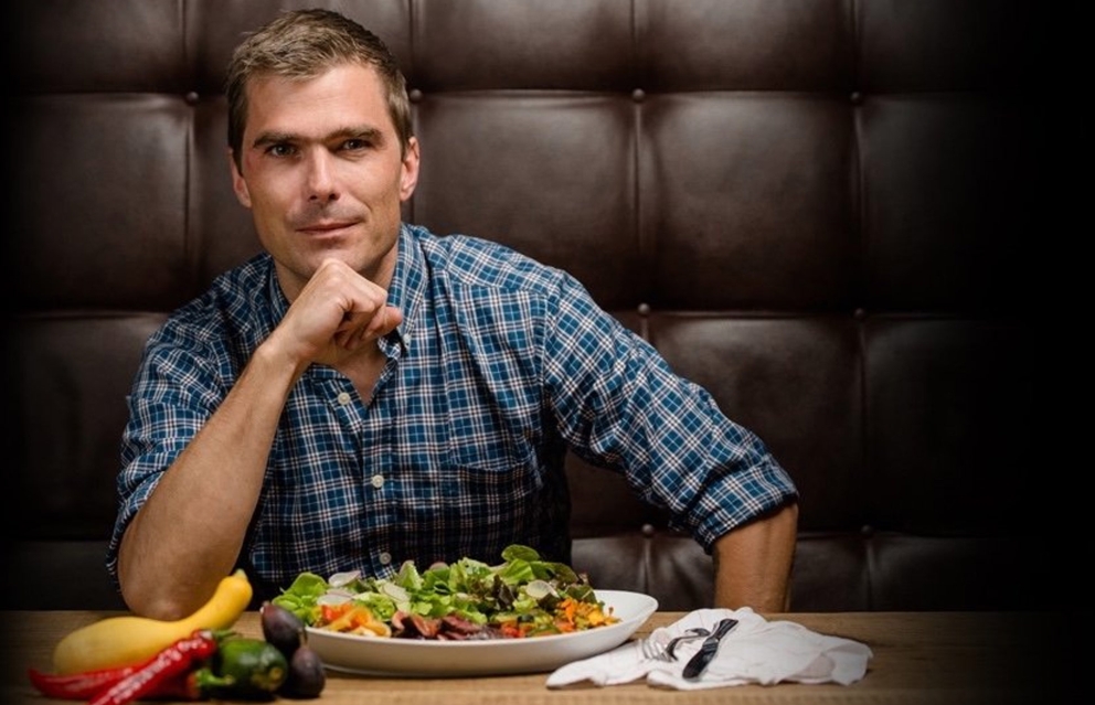 A headshot of chef Hugh Acheson sitting down to eat a plate of salad.