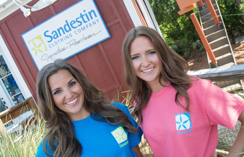 Two women posing outside of Sandestin Clothing Company in branded shirts