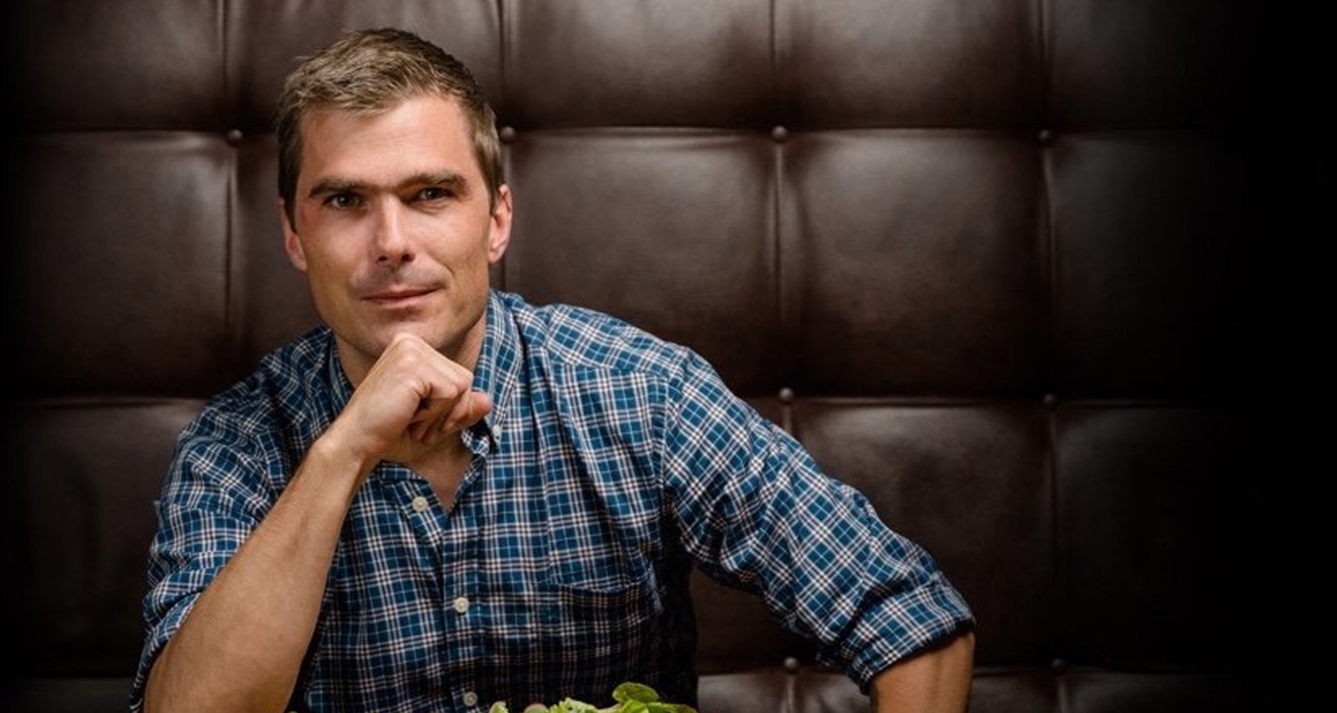A headshot of chef Hugh Acheson sitting down to eat a plate of salad.