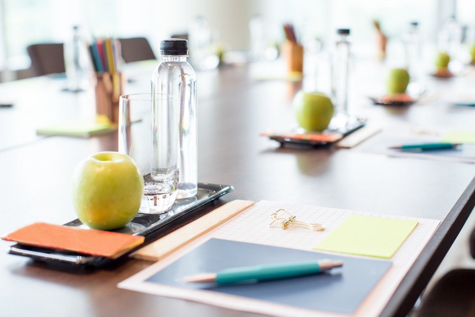 A table set for a business meeting with a pen, pad of paper, apple, and bottle of water