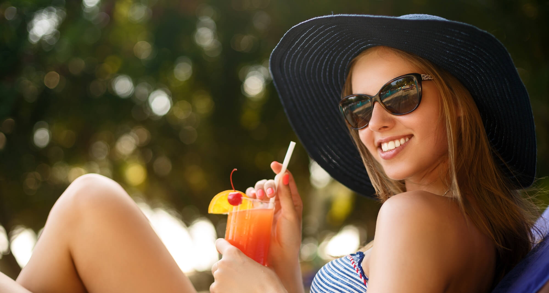 A young woman relaxing in a big sun hat sipping a cocktail.