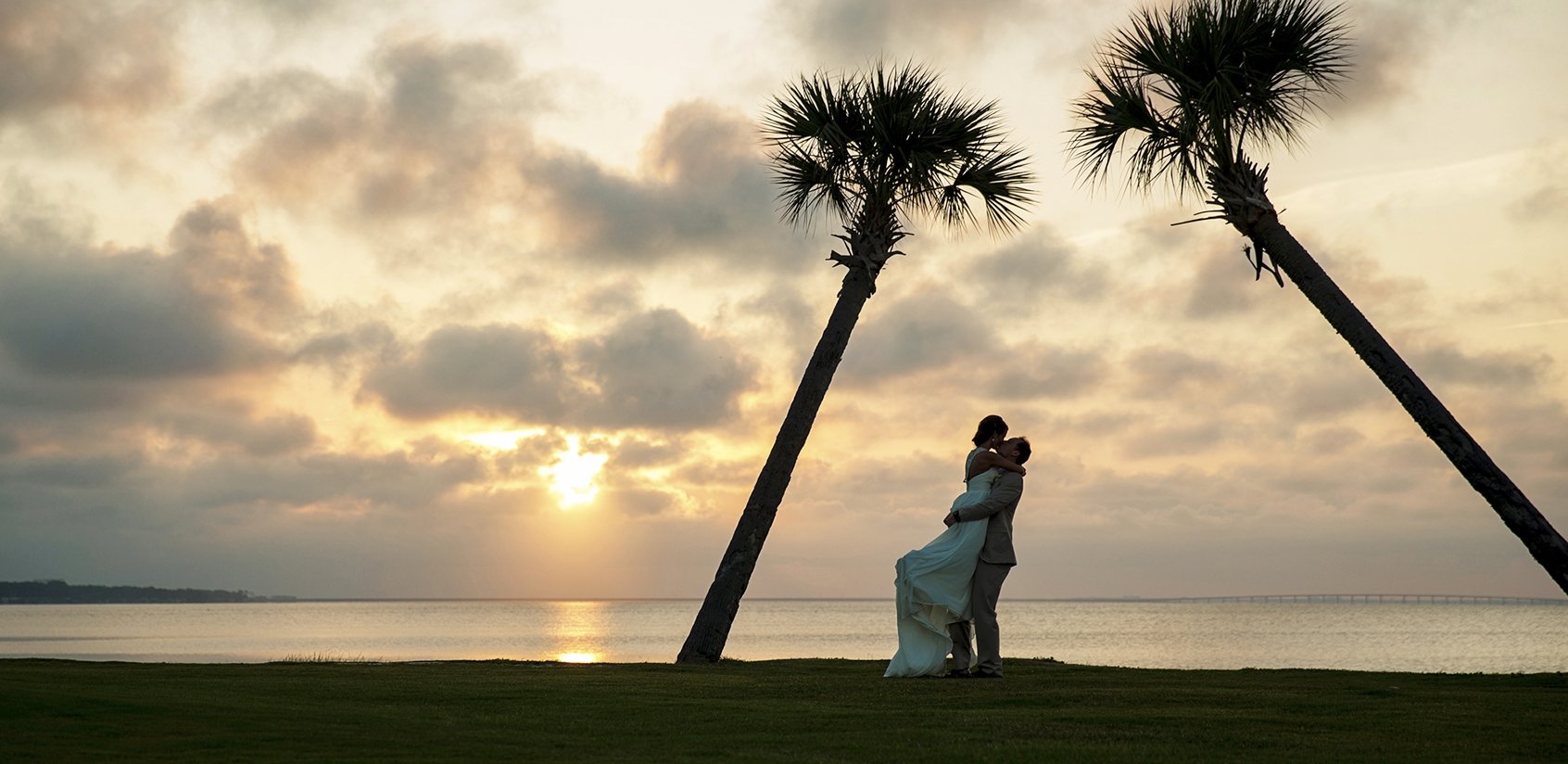 A newly wed couple kissing on the beach with palm trees 