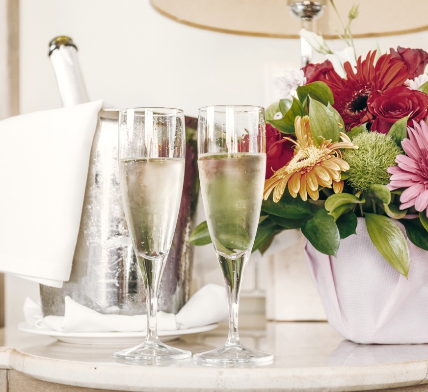 two champagne glasses and flowers on a nightstand.