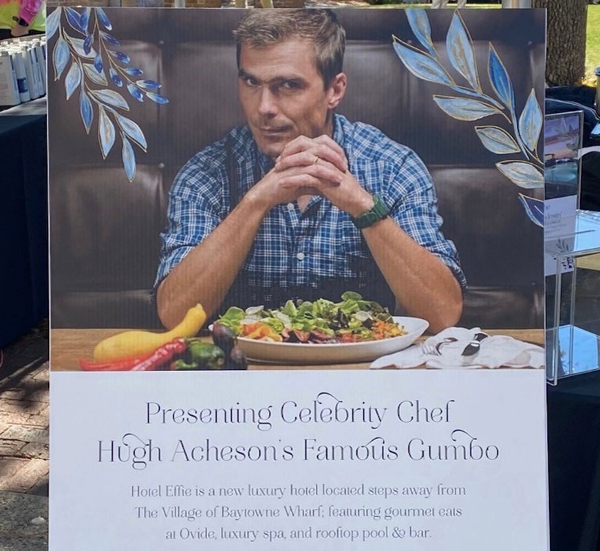 A poster at an outdoor booth that reads, Presenting Celebrity Chef Hugh Acheson's Famous Gumbo.
