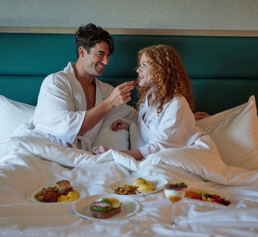 A man and woman wearing robes eating breakfast in bed.
